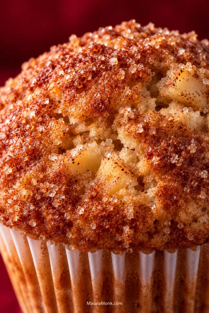 Extreme close-up of a golden muffin crown with cinnamon, small surface cracks and scattered coarse sugar crystals.