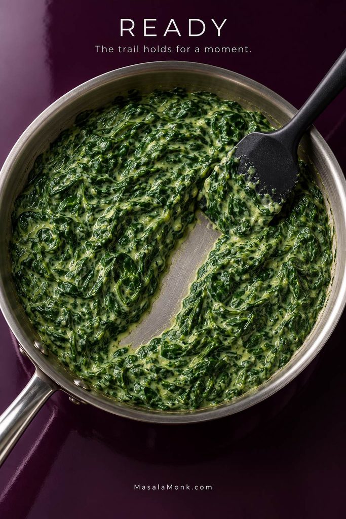 Spatula drawn through finished creamed spinach, leaving a temporary open trail that exposes the bottom of the skillet.