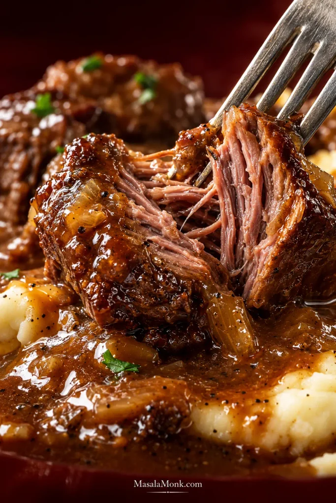 Close-up of a fork opening a gravy-coated piece of braised beef and exposing moist brown fibers inside.