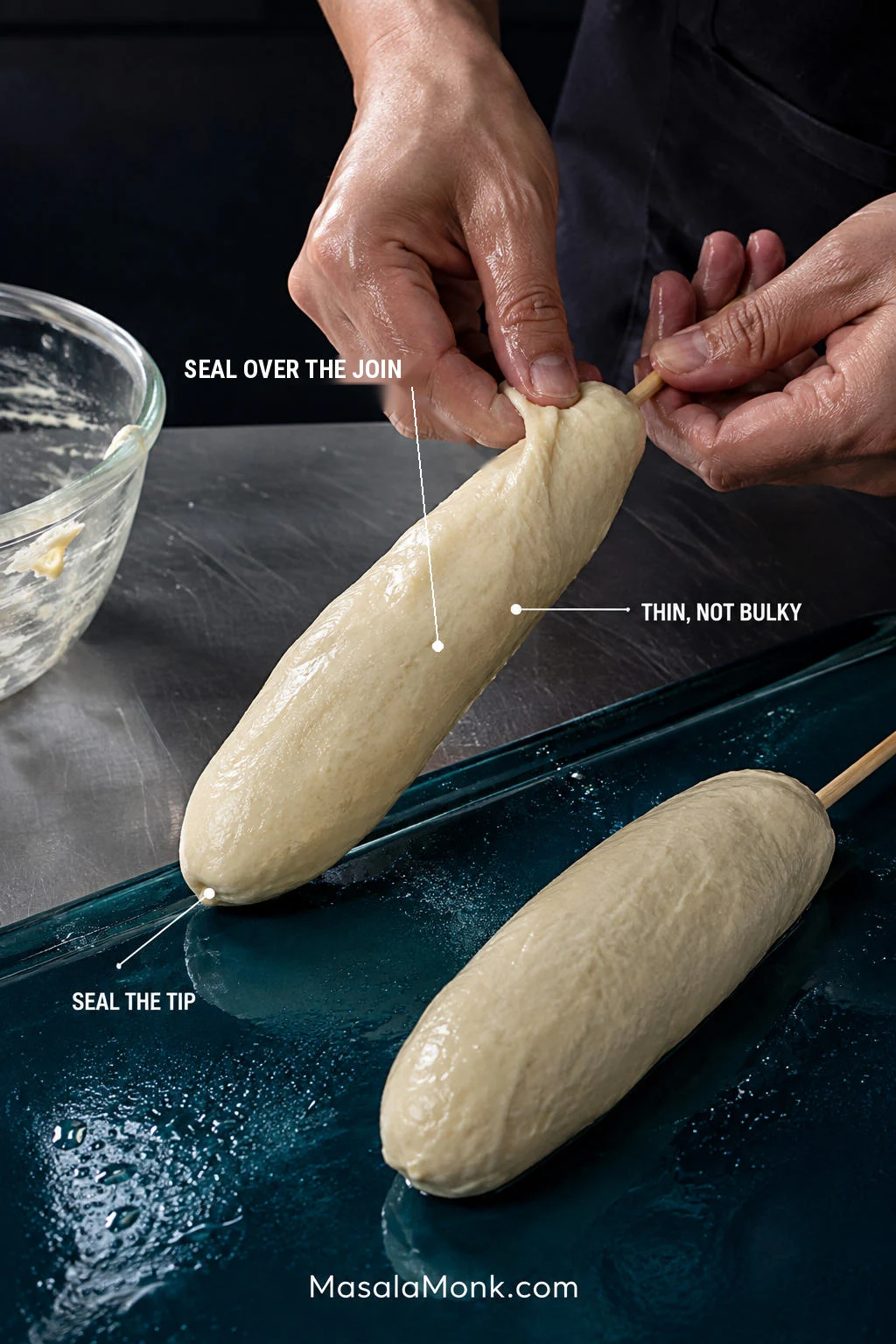 Hands wrapping sticky dough around a sausage-and-mozzarella skewer, showing a thin coating with the tip and filling join fully covered.