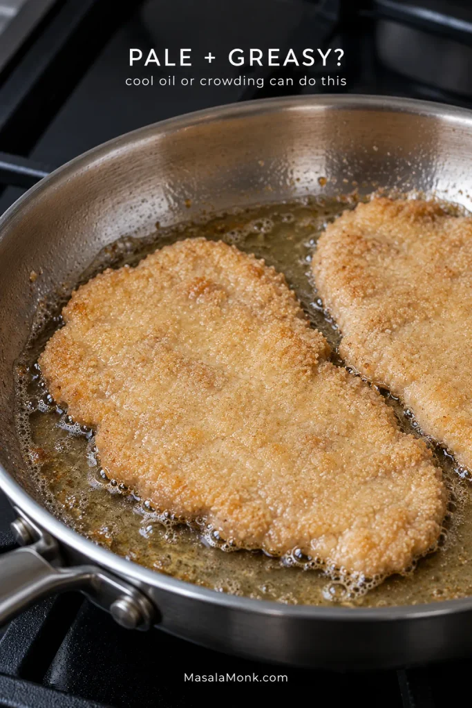 Two pale breaded pork schnitzels crowded in shallow oil in a stainless-steel skillet, with a glossy surface and relatively weak bubbling.