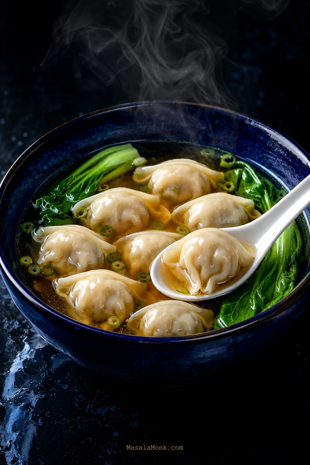 Steaming bowl of pork-and-shrimp wonton soup with clear amber broth, baby bok choy, sliced scallions and a wonton lifted on a white spoon.
