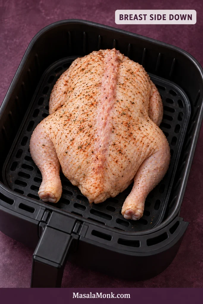 Seasoned whole chicken positioned breast-side down in an air-fryer basket with the back facing upward.