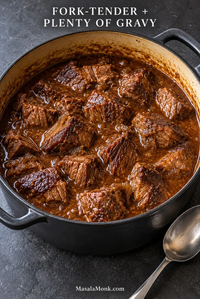 Large intact pieces of braised beef tips surrounded by brown gravy in a heavy Dutch oven.