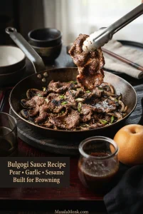 Thin browned bulgogi beef with onions, scallions and sesame in a skillet, beside a jar of dark sauce and a round Asian pear.