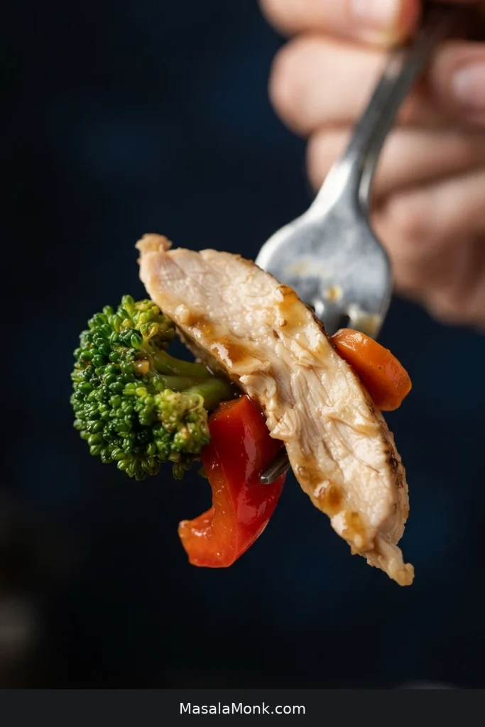 Close-up bite of sliced chicken, broccoli and red bell pepper with a thin translucent brown sauce.