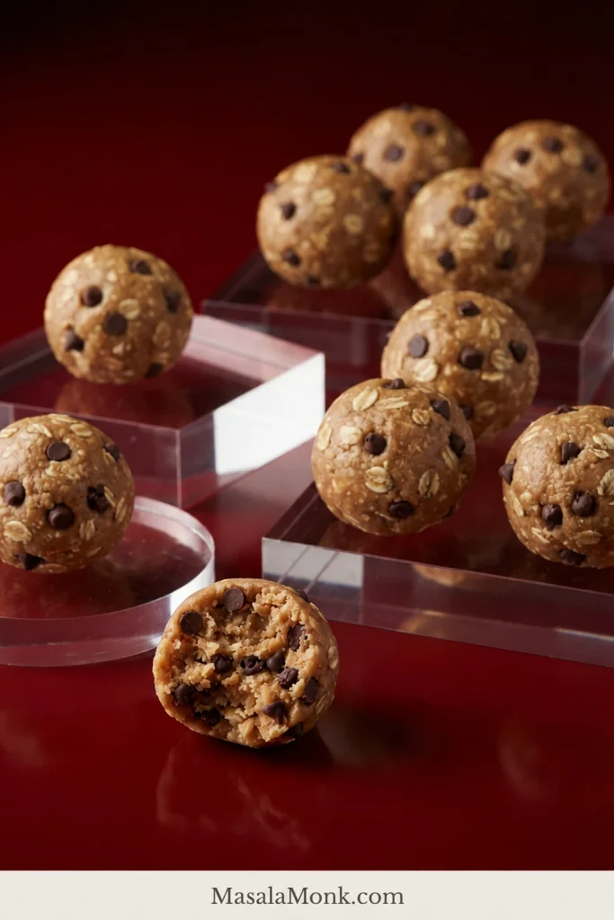 Chocolate-chip oatmeal peanut butter balls arranged on clear risers, including one split open to show mini chocolate chips mixed through the oat and peanut butter center.