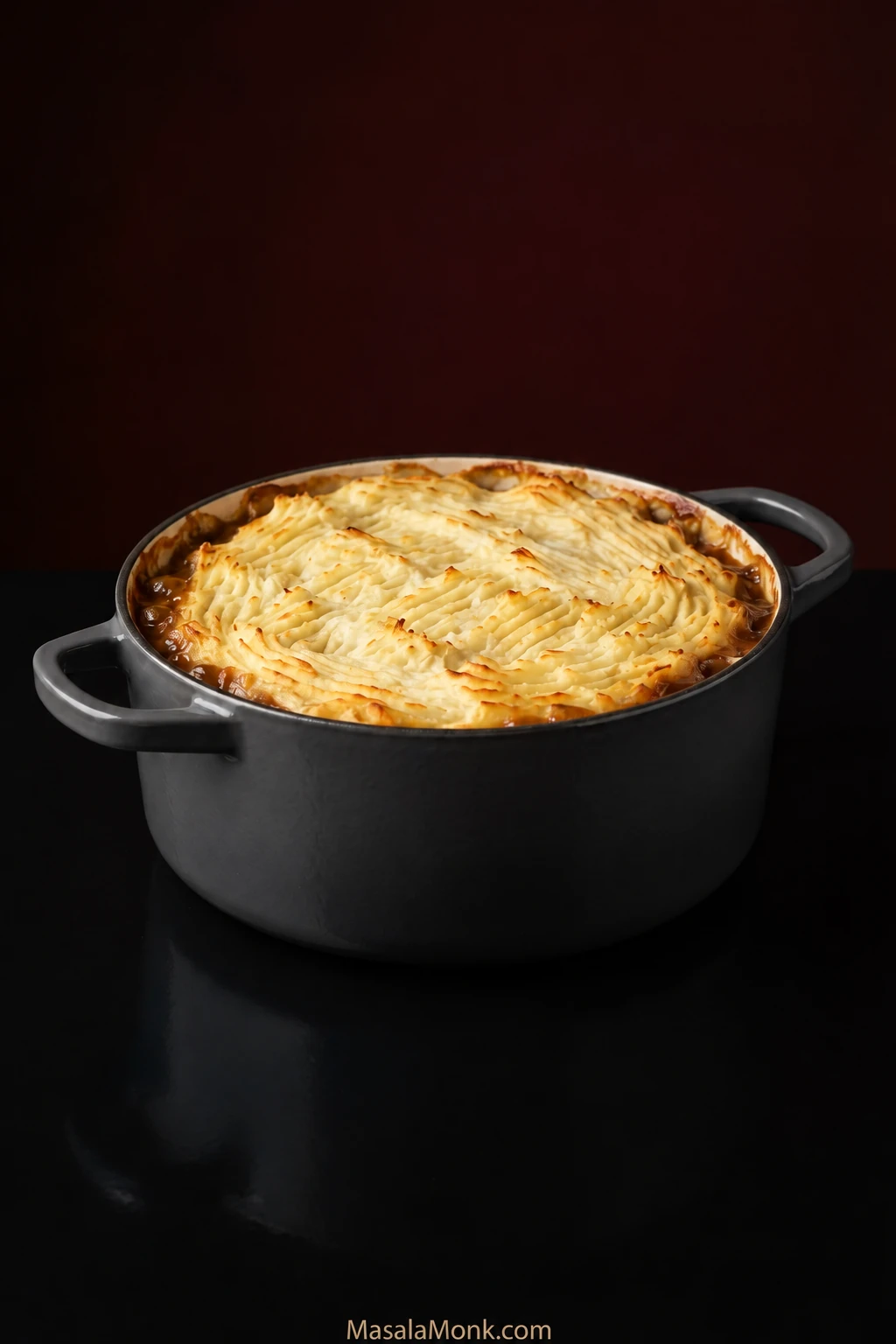 Whole cottage pie in a dark casserole with fork-ridged mashed potato browned on the peaks and brown gravy visible around the inner rim.