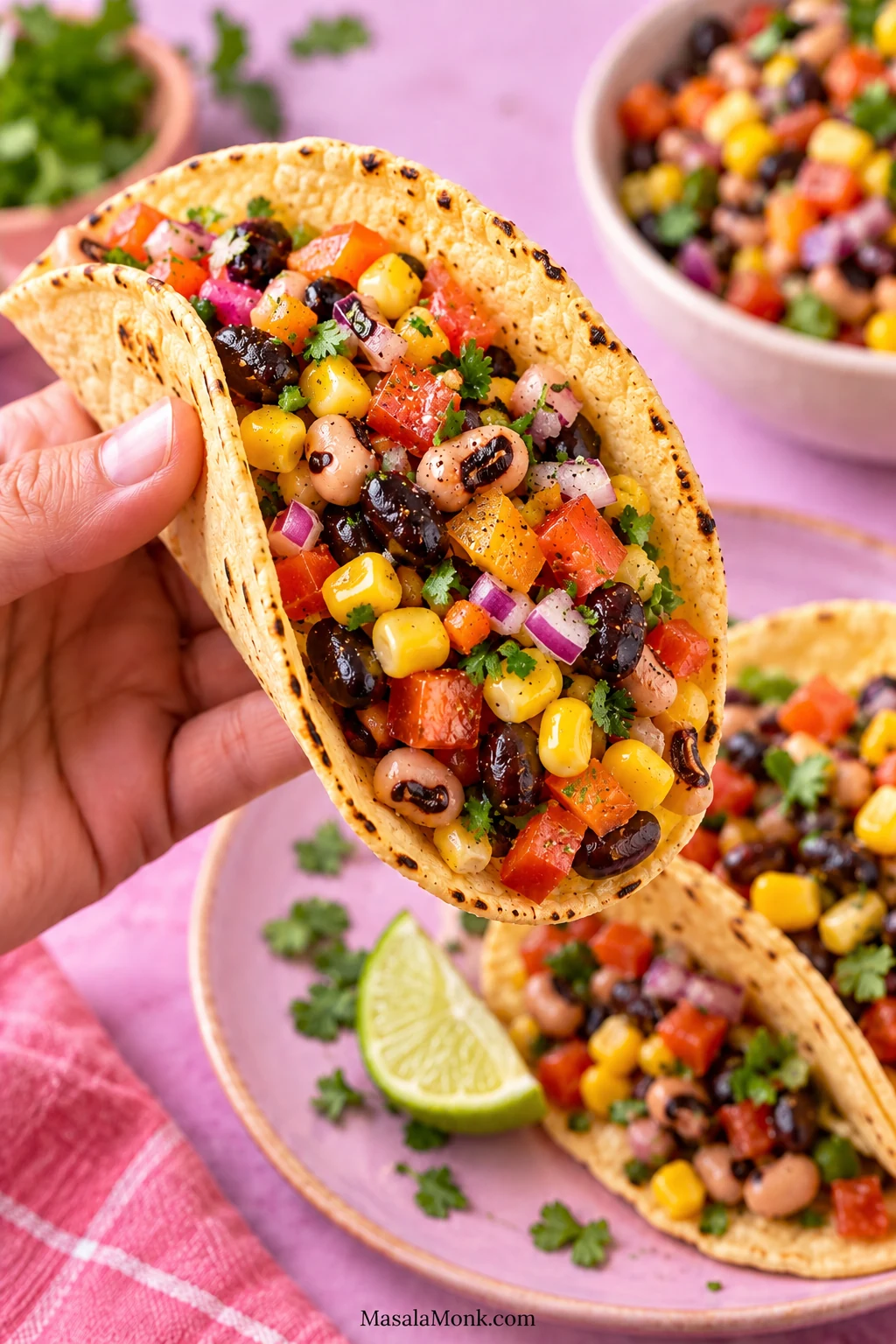 A hand holding a corn tortilla taco filled with Cowboy Caviar made from black-eyed peas, black beans, corn, tomato, bell pepper, red onion and cilantro.