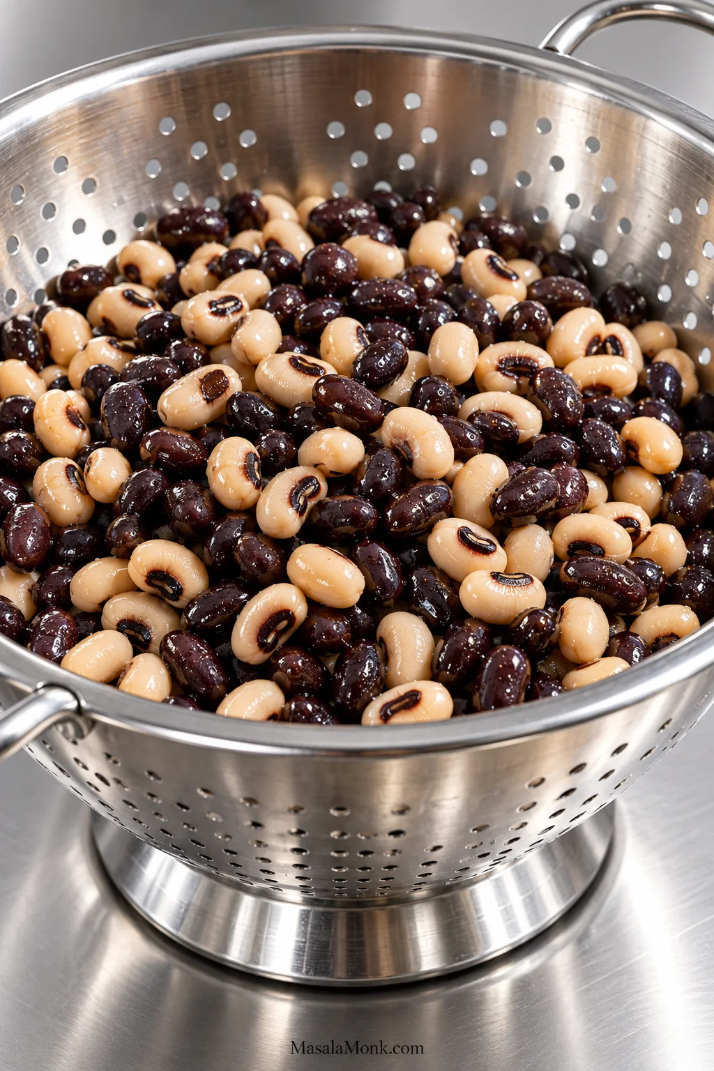 Rinsed black-eyed peas and black beans resting in a stainless steel colander with slight surface moisture and no visible pooled liquid.
