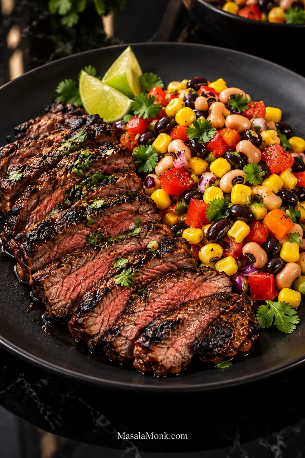 Sliced charred carne asada served beside Cowboy Caviar with black-eyed peas, black beans, corn, tomato, bell pepper, red onion, cilantro and lime wedges.