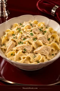 Creamy Crock Pot chicken and extra-wide egg noodles with chunky chicken pieces in a dark serving bowl.
