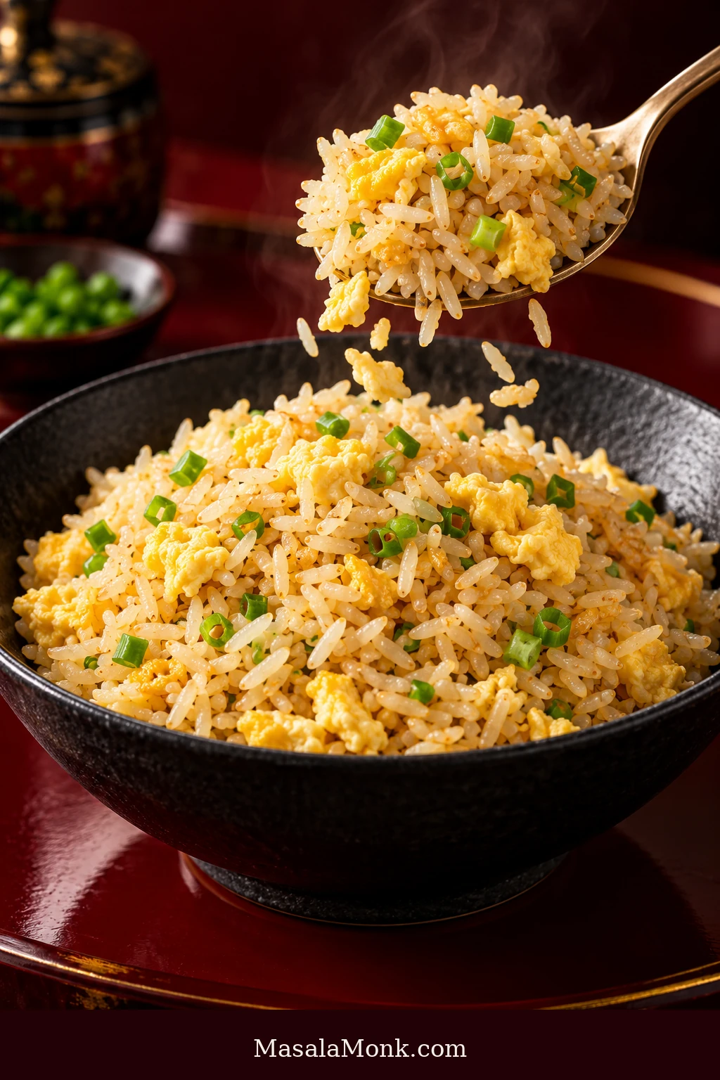 Dark bowl of pale golden egg fried rice with separate jasmine grains, soft yellow egg curds and sliced scallions, while a serving spoon lifts rice and several grains fall back toward the bowl.