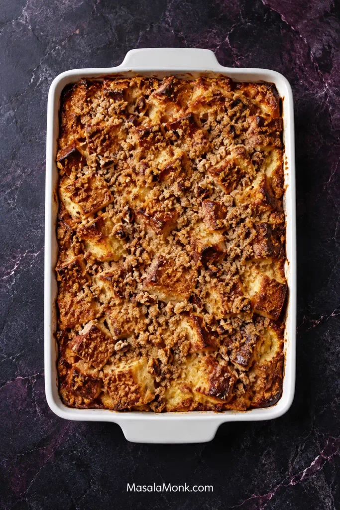Overhead view of a rectangular French toast casserole with irregular golden bread pieces and browned crumble across the surface.