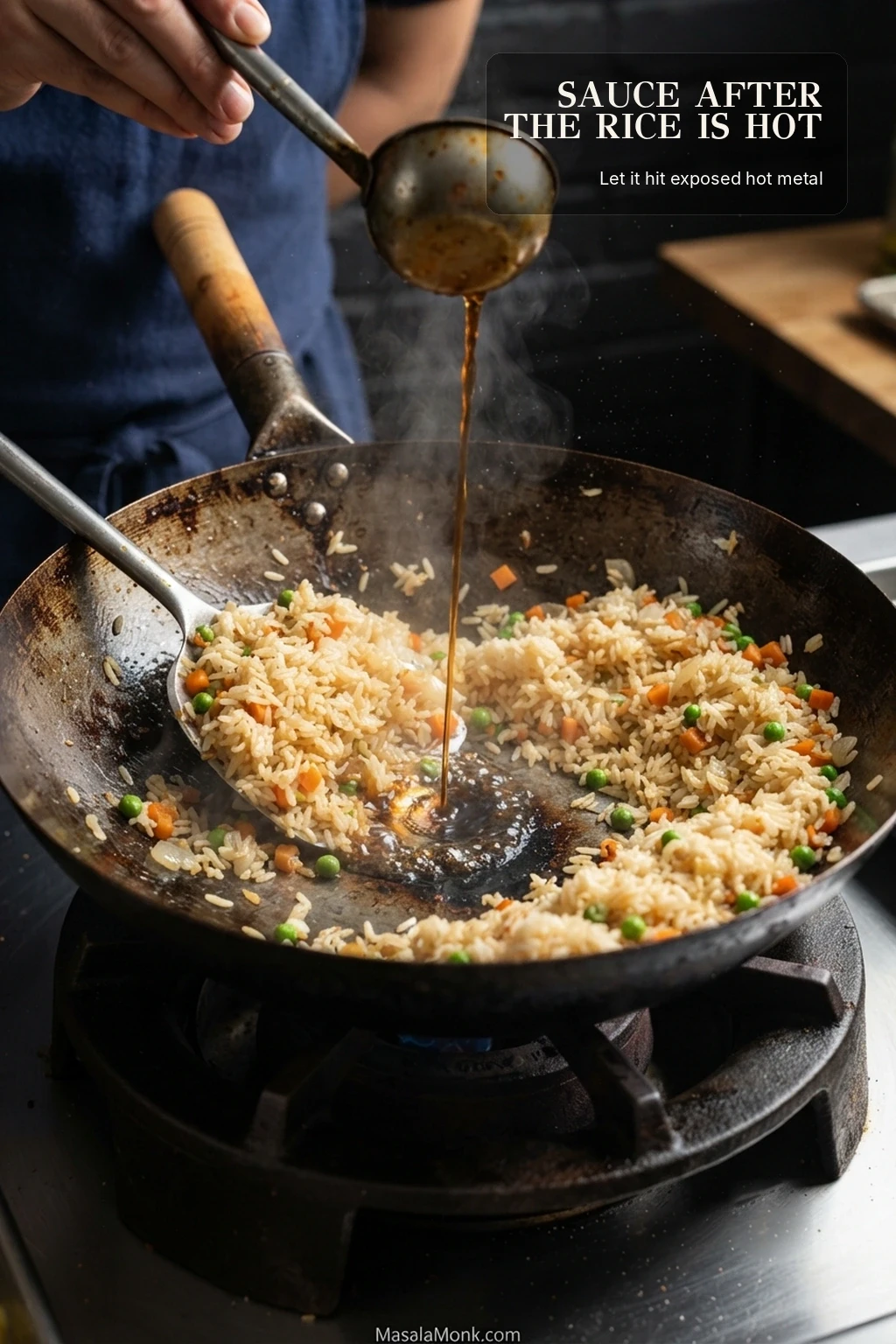 Hot rice and vegetables pushed aside in a wok while a small stream of brown seasoning sauce is poured onto exposed hot metal.