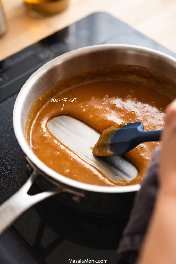 Caramel custard in a stainless saucepan with a spatula leaving a clean trail that is beginning to close at the edges.