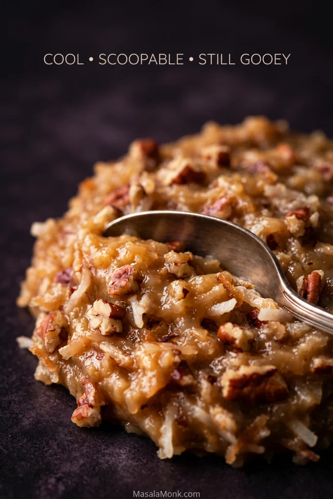 Close-up of cooled coconut-pecan frosting with a spoon pressing into a soft, moist mound that holds its shape.