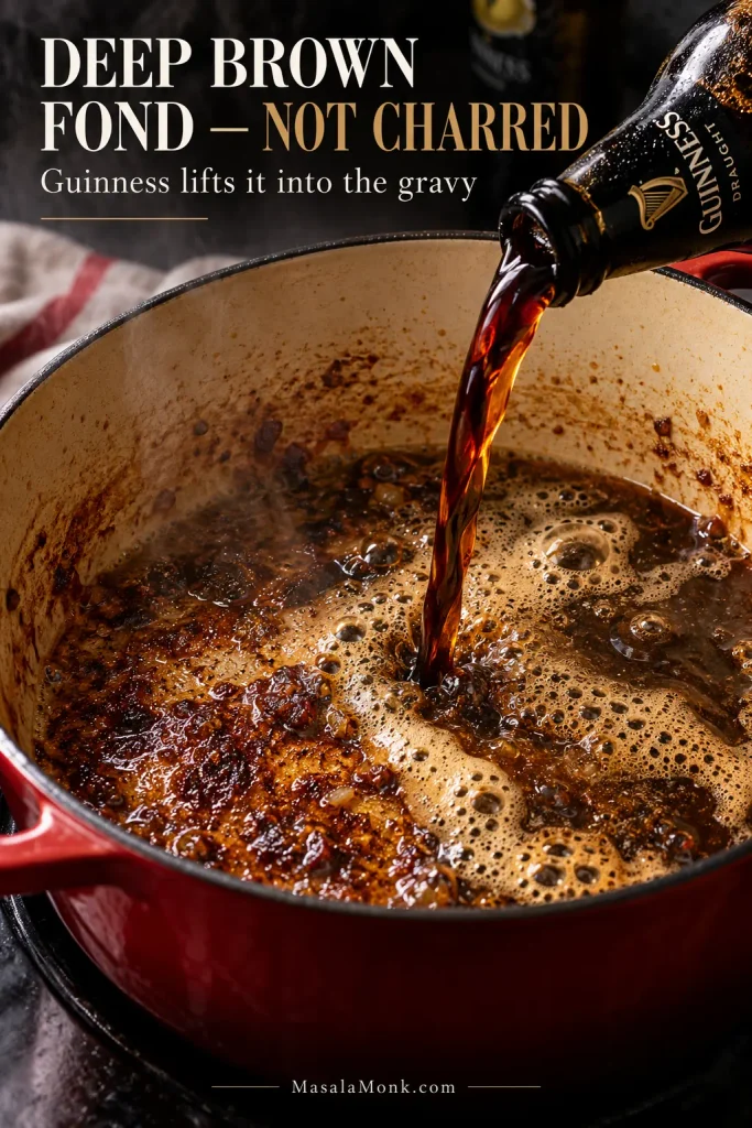 Dark stout being poured into a red Dutch oven while browned fond loosens from the bottom of the pot.