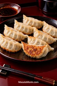 Pan-fried Japanese gyoza on a dark plate with pale pleated wrappers and golden crisp bases, including one dumpling turned to reveal its browned underside.