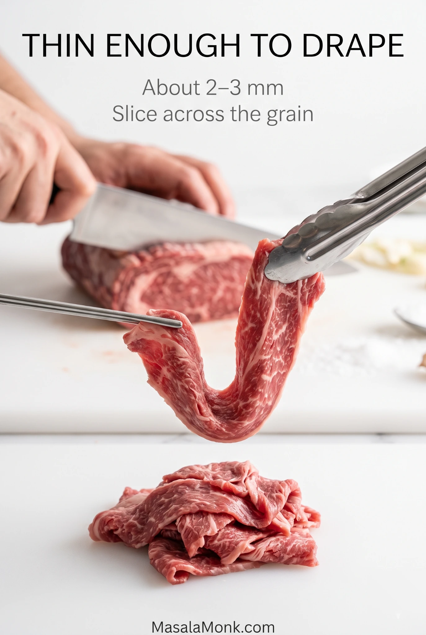 Very thin raw beef slice hanging in a soft U-shaped drape from metal tongs, with more thin slices and a knife cutting beef in the background.