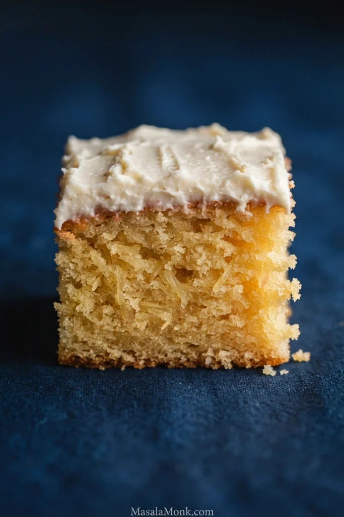 Close side view of golden pineapple cake with an evenly baked tender crumb, small pineapple pieces and white cream cheese frosting.