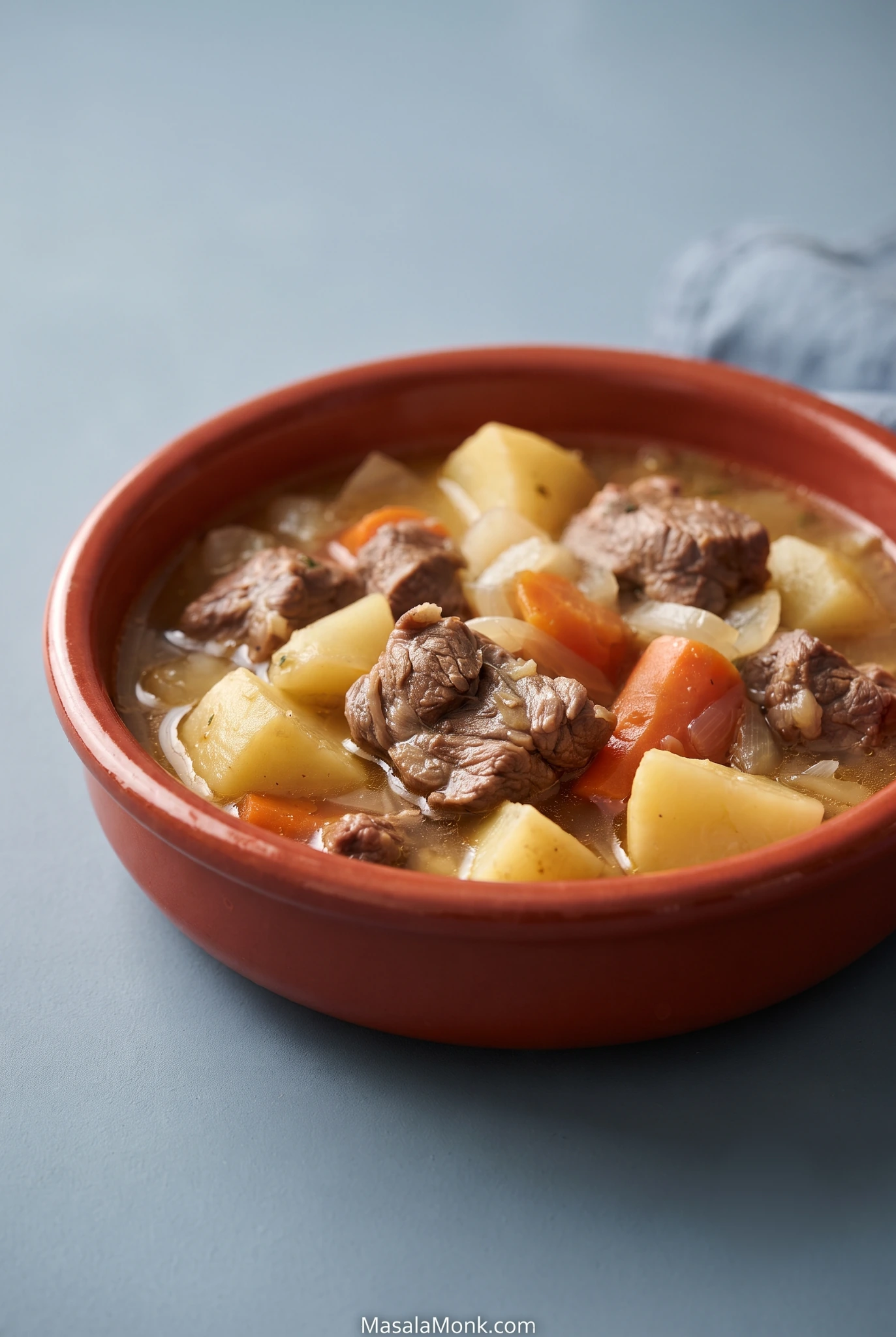 Terracotta bowl of Irish lamb stew with tender lamb shoulder, large potato chunks, carrots and softened onions in a light golden broth.
