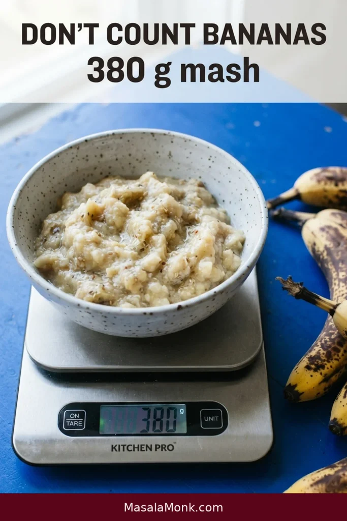 A bowl of mashed ripe banana sits on a digital scale displaying 380 g beside whole bananas of different sizes.