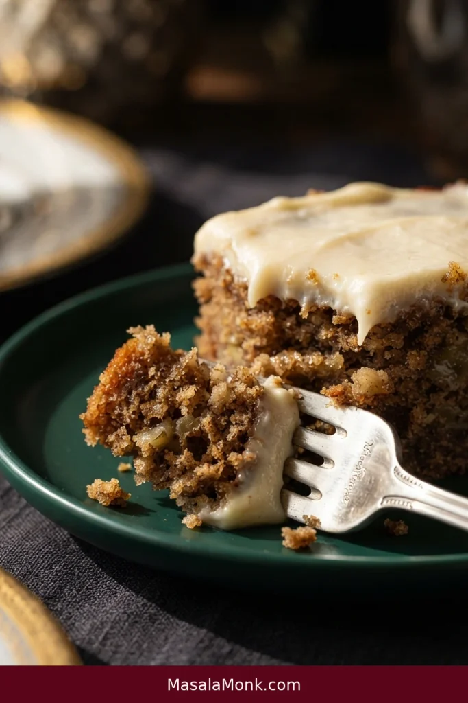 A silver fork lifts a bite from a frosted banana cake square, exposing its golden interior.