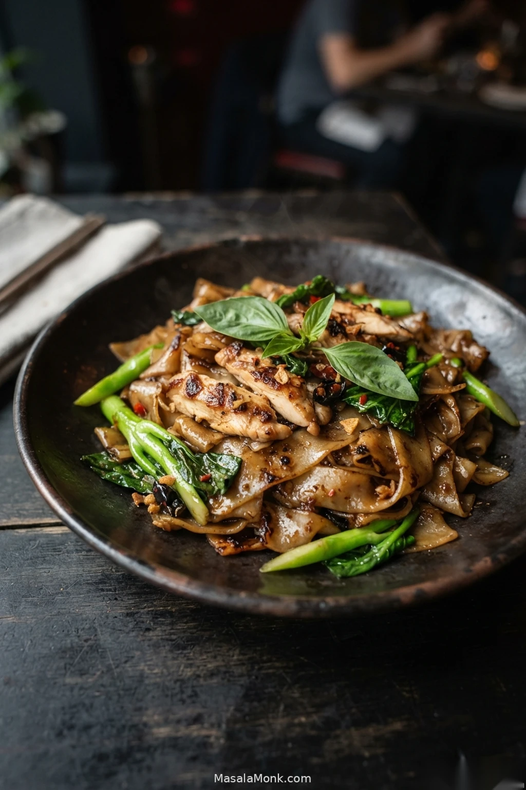 Finished Pad Kee Mao with glossy wide rice noodles, sliced chicken, Chinese broccoli, red chilli and fresh basil.