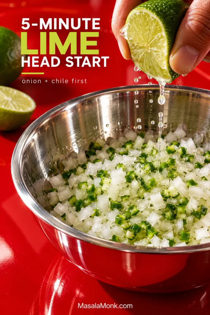 Fresh lime being squeezed over finely diced white onion and minced green chile in a stainless-steel bowl.