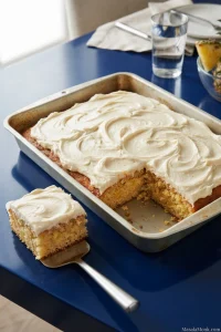 Square slice of golden crushed-pineapple sheet cake with white cream cheese frosting beside the remaining rectangular cake.