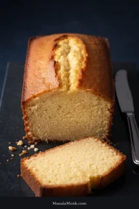 Golden loaf-style pound cake with a long center crack, cut open to reveal an even pale-yellow crumb, with one thick slice in front.