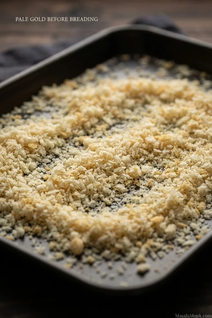 Light-golden panko spread across a dark baking sheet; on-image text reads “Pale gold before breading.”