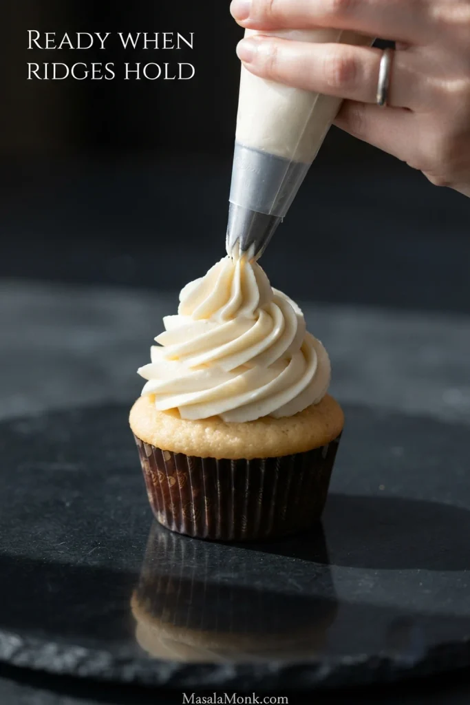Whipped cream cheese frosting being piped into a tall swirl with clearly defined ridges that hold their shape.