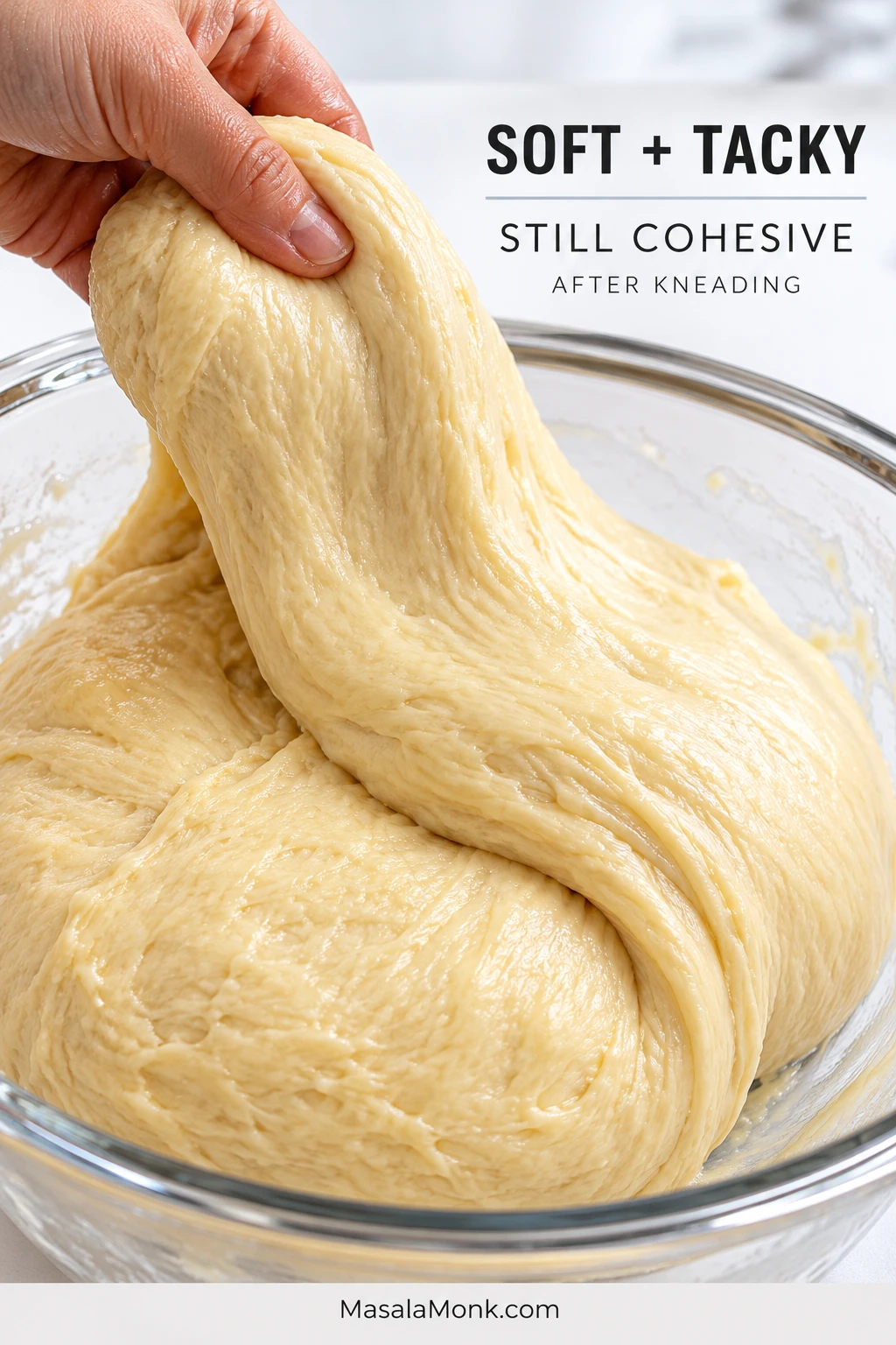A hand lifts one broad fold of soft, moist beignet dough from a glass bowl; the dough stretches slightly while remaining one cohesive mass. Text reads “Soft + Tacky” and “Still Cohesive.”