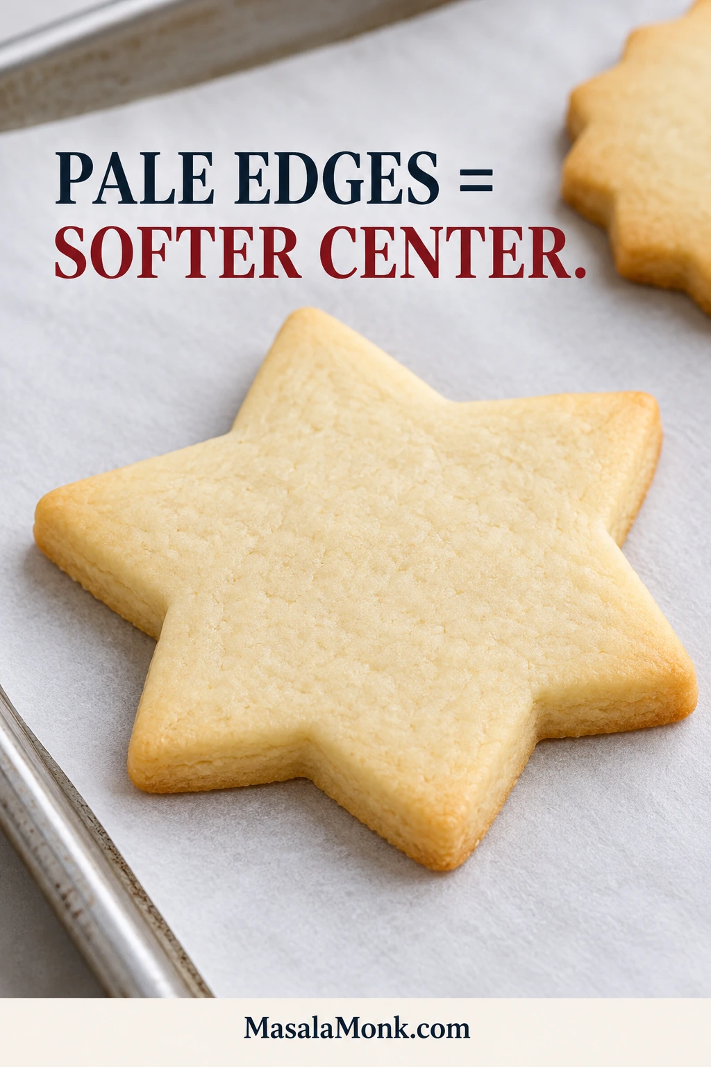 Close-up of a pale baked star sugar cookie with a matte top and set edge on parchment over a metal baking sheet.