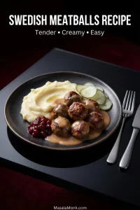 Small Swedish meatballs with creamy brown gravy and mashed potatoes, served with ruby lingonberry preserves and thin pickled cucumber slices on a dark plate.