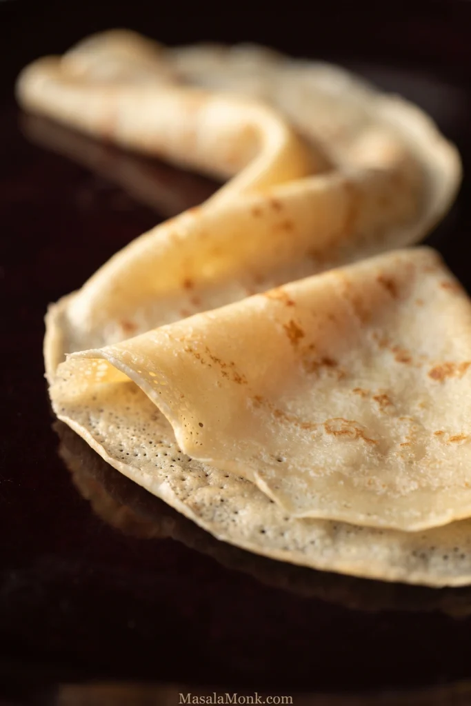 Close-up of a very thin pale-golden crepe draped into soft folds, showing fine layered edges and light brown cooking marks.