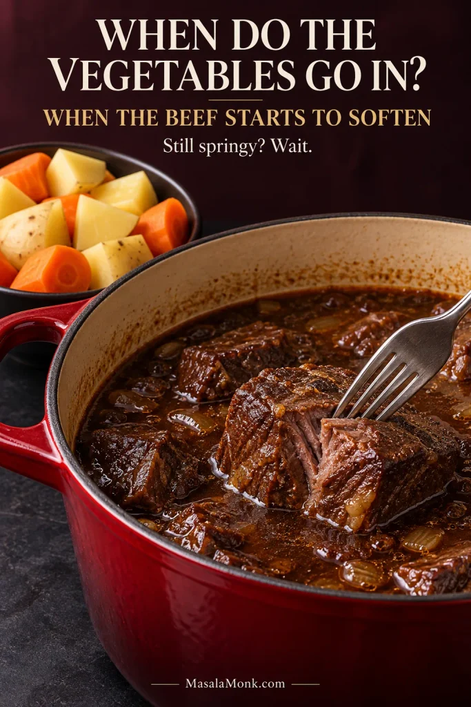 Fork testing a large partially tender beef piece in a Dutch oven while cut potatoes and carrots wait beside the pot.