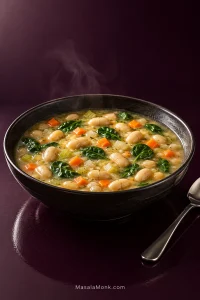 Dark bowl filled with creamy white bean soup, whole cannellini beans, diced carrots and celery, and wilted spinach.